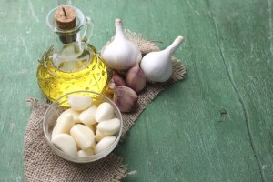 Fresh sliced garlic in glass bowl and oil in glass bottle, on wooden background