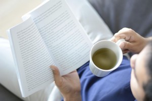 A man reading book with hot tea cup in another hand