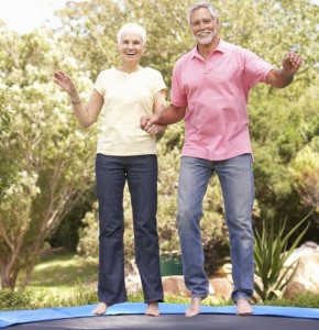 Senior Couple Jumping On Trampoline In Garden
