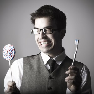 Happy smart young man with a lollipop in one hand and a toothbru