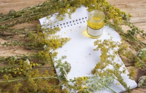 massage oil in a glass bottle, herbs and notepad on wooden table
