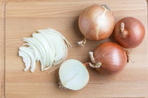 Whole and sliced onions on wooden cutting board